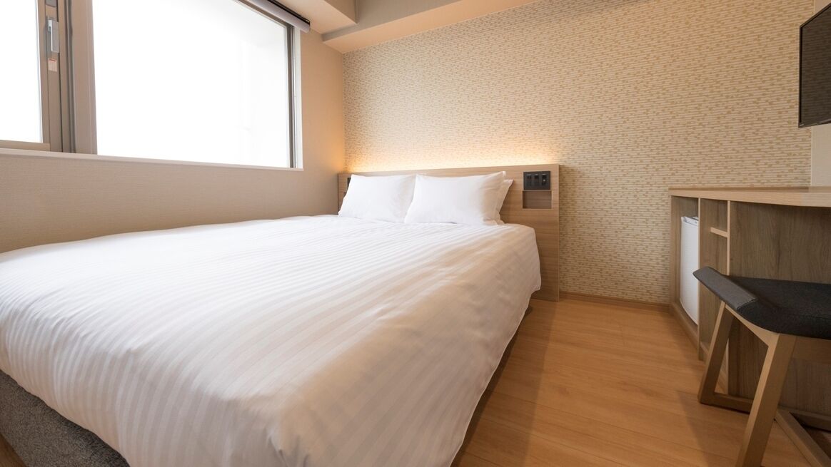 A hotel room with a large bed, a desk, and a wall-mounted light.