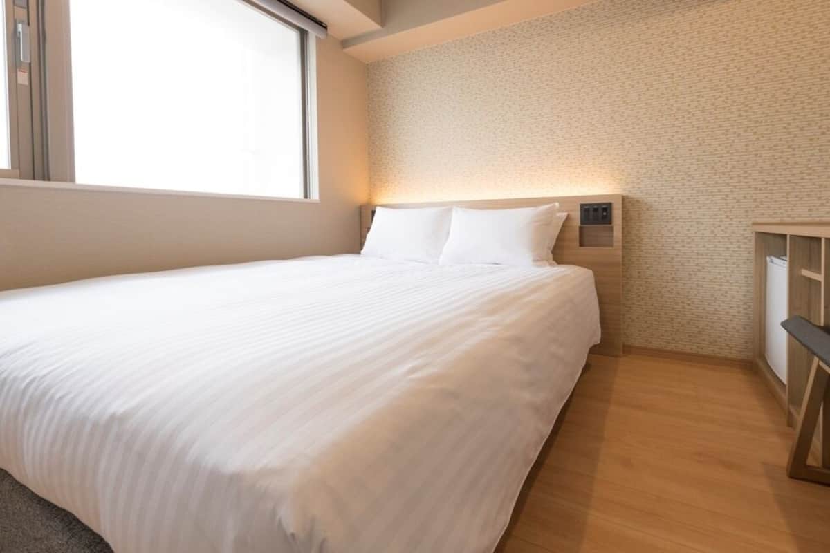 A hotel room with a large bed, a desk, and a wall-mounted light.