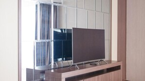Quarto moderno com piso de madeira, um espelho grande e uma TV de tela plana sobre um console de madeira.