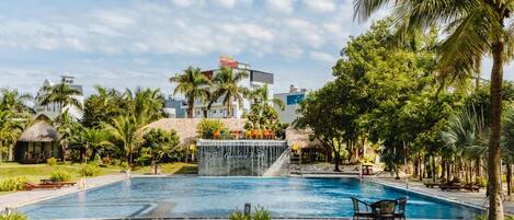 A swimming pool with a waterfall feature, surrounded by palm trees and a well-maintained lawn.
