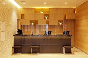 A modern reception desk with a marble top, wooden shelving above, and a security camera above. - JR Inn Sapporo N2 (Sapporo)