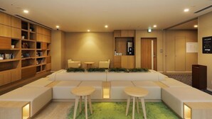 A modern lounge area with a sofa, two chairs, a coffee table, and a bookshelf. - JR Inn Sapporo N2 (Sapporo)
