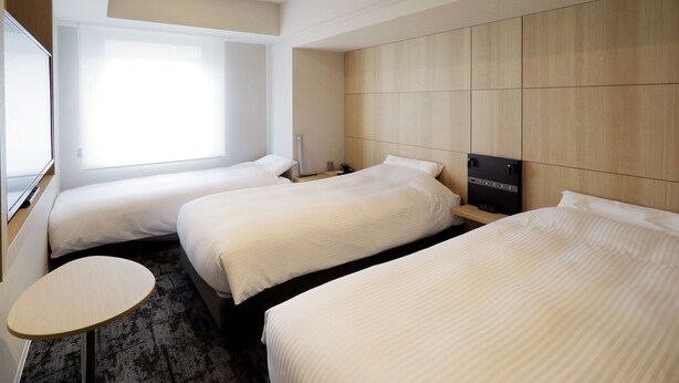 A hotel room with two single beds, a small round table, and a large window providing natural light. - JR Inn Sapporo N2 (Sapporo)