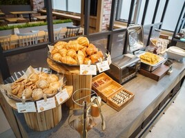 Una vitrina de panadería con diversos productos horneados como croissants y pasteles, con etiquetas de precio y una máquina de café al fondo.