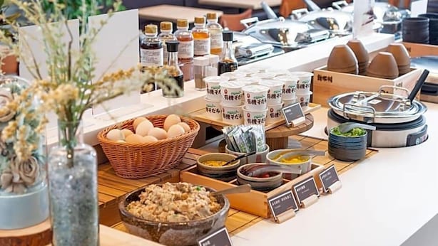 A buffet setup with various food items, condiments, and a wicker basket of eggs. - Super Hotel Okayama (Okayama)