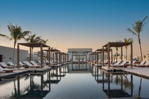 A pool area with lounge chairs and umbrellas, surrounded by palm trees and modern buildings. - Alila Hinu Bay Salalah Mirbat (Mirbat)