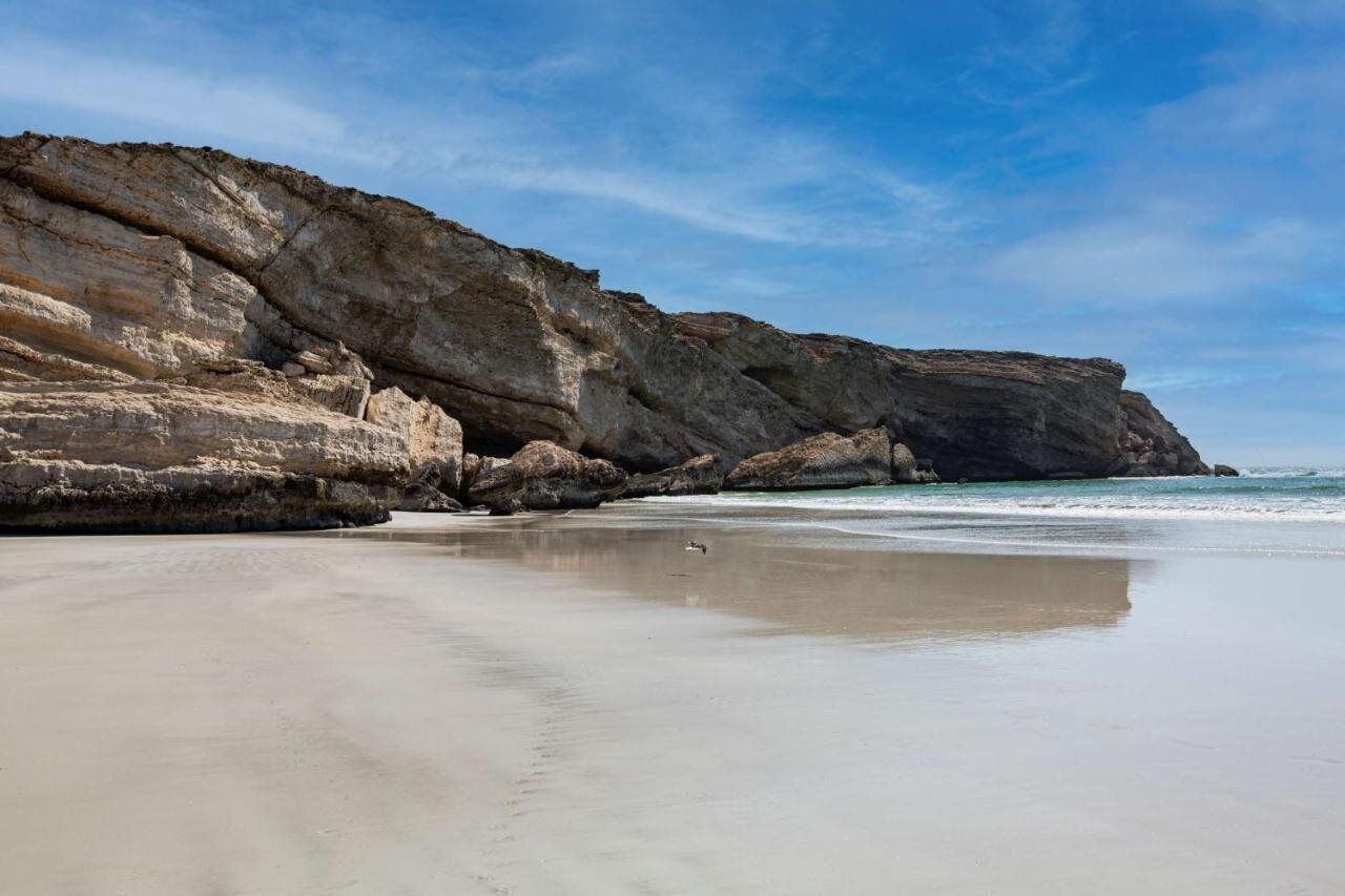 Uma praia com um penhasco rochoso e mar calmo.