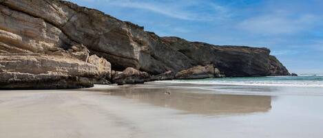 Uma praia com um penhasco rochoso e mar calmo.
