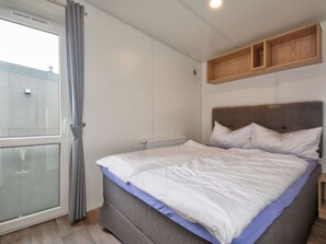 Ein Schlafzimmer mit einem Bett, einem Fenster mit Vorhängen, einem Heizkörper und einem Holzregal über dem Bett.