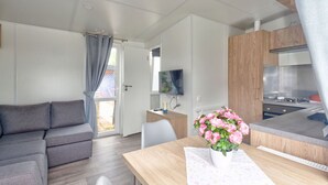 Un espai vital modern i compacte amb un sofà, una taula de dinar amb un ram de flors, una zona de cuina i una televisió.