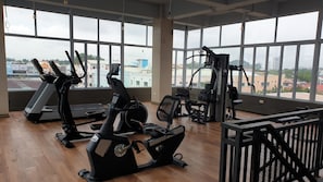 Ein Fitnessstudio mit mehreren Trainingsgeräten, großen Fenstern und Blick auf Gebäude.