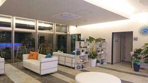 Un hall d’entrée moderne avec un canapé blanc, un espace salon circulaire et une étagère pour plantes.