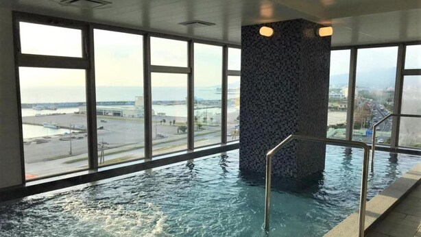 Une piscine intérieure dotée de grandes fenêtres qui offrent une vue sur un plan d’eau et des bâtiments éloignés.