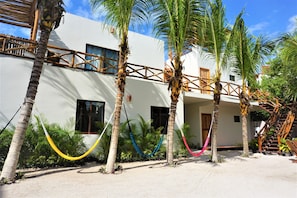 A white building with multiple windows, a wooden balcony, and several palm trees. - La Puerta Azul Beachfront - Adults Only (Isla Holbox)