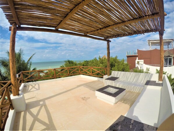 A covered outdoor area with a wooden railing, a white cushioned seating area, and a view of the ocean. - La Puerta Azul Beachfront - Adults Only (Isla Holbox)
