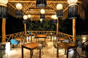 An outdoor dining area with wooden tables and chairs, thatched roof, and hanging light fixtures. - La Puerta Azul Beachfront - Adults Only (Isla Holbox)