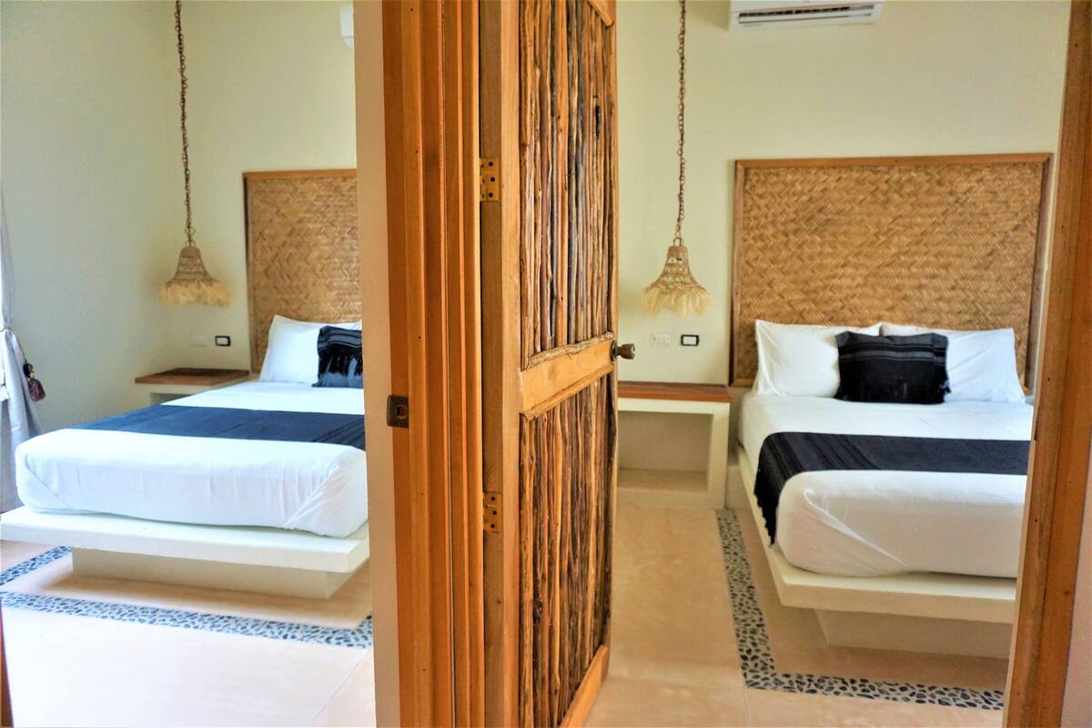 A hotel room with two beds, each with a wooden headboard, white bedding, and a hanging lamp.