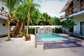 A pool area with a stone wall, palm trees, and a wooden staircase. - La Puerta Azul Beachfront - Adults Only (Isla Holbox)