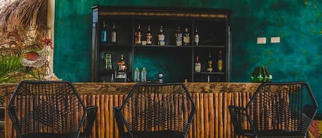 A bar area with a bamboo backdrop, hexagonal chairs, and a shelf of liquor bottles.