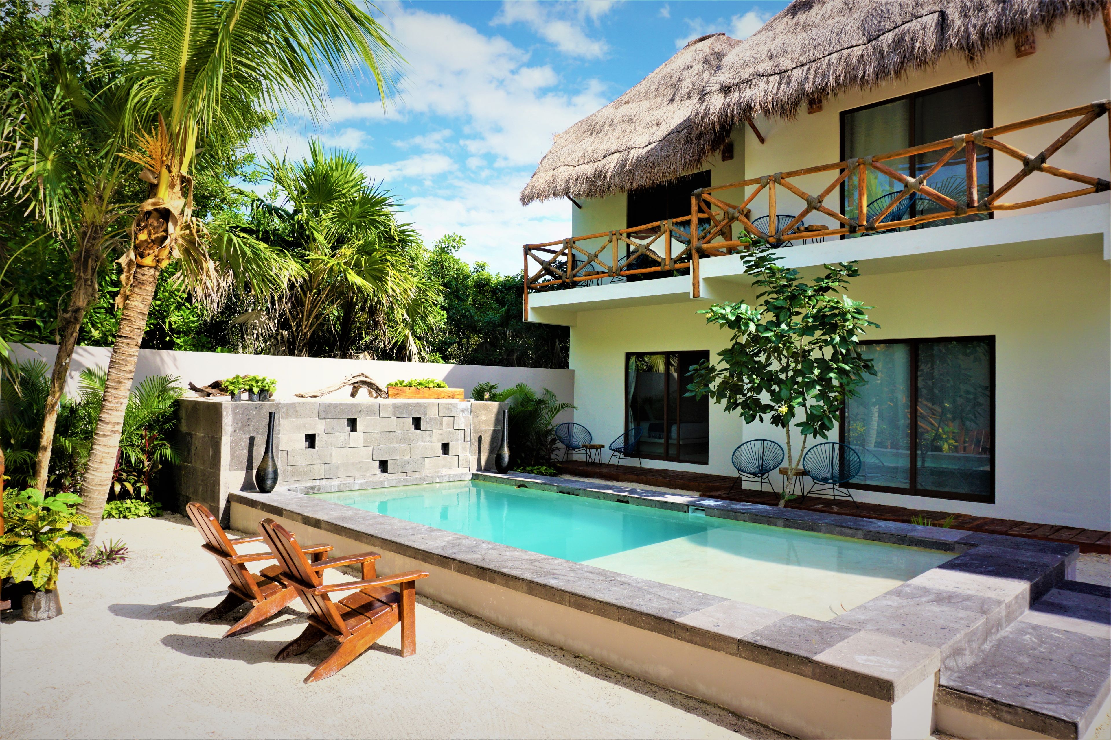 A two-story house with a pool, wooden deck chairs, and a thatched roof balcony.
