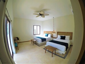 Ein Hotelzimmer mit zwei Betten, einem Deckenventilator, einem kleinen Tisch und einem Fenster.