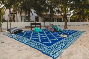 A beach setting with a patterned blue mat, a chair, and a small table. - La Puerta Azul Beachfront - Adults Only (Isla Holbox)