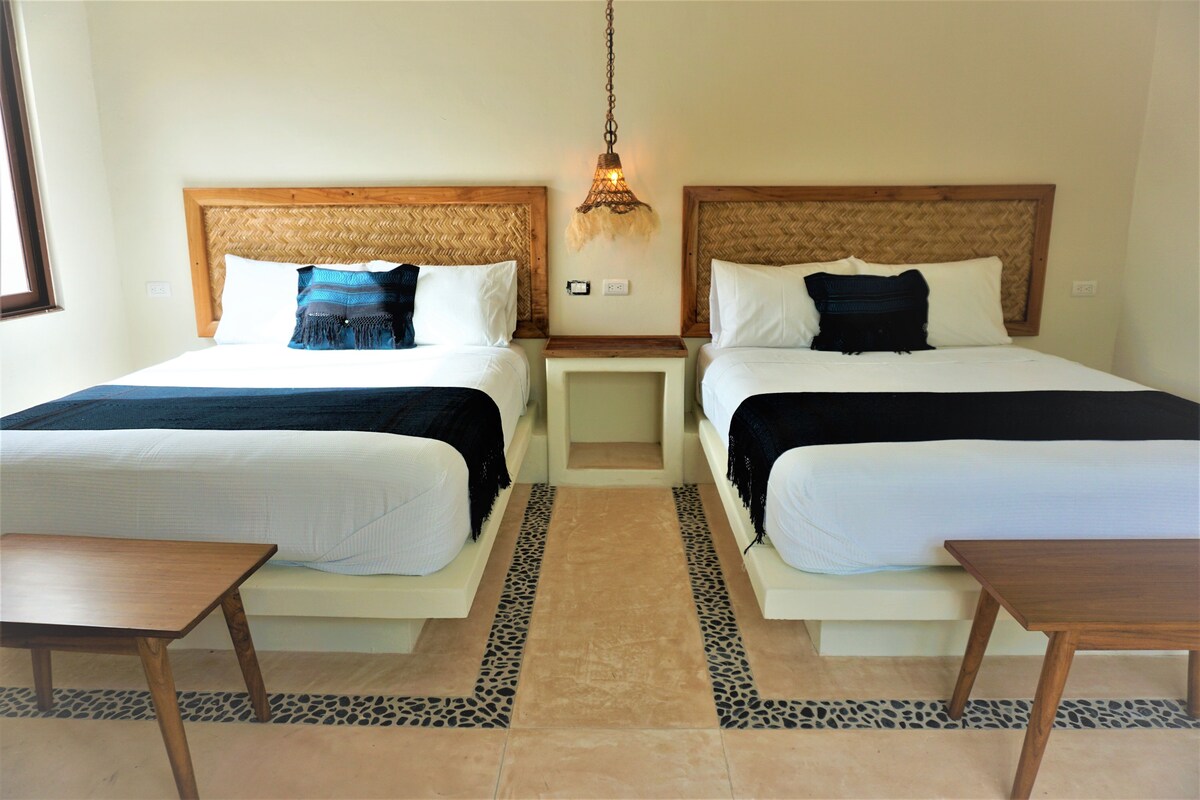 A hotel room with two beds, a small table, and a nightstand.