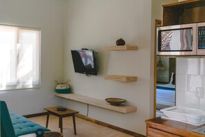 A living room with a sofa, a coffee table, a TV, and wooden shelves with decorative items. - La Puerta Azul Beachfront - Adults Only (Isla Holbox)