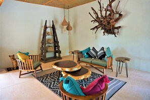 A cozy living area with a wooden chair, sofa, and round wooden table. - La Puerta Azul Beachfront - Adults Only (Isla Holbox)