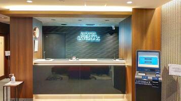 A hotel reception area with a modern design, including a reception desk, a digital screen, and a sign indicating the hotel name 'HOTEL LIVENMAX'.