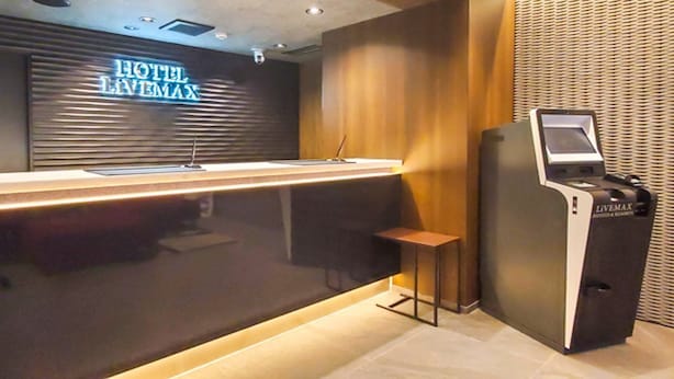 Egy modern stílusban berendezett szállodai recepciós tér, mely tartalmaz egy recepciós pultot, egy ülősarokot és egy önkiszolgáló terminált.