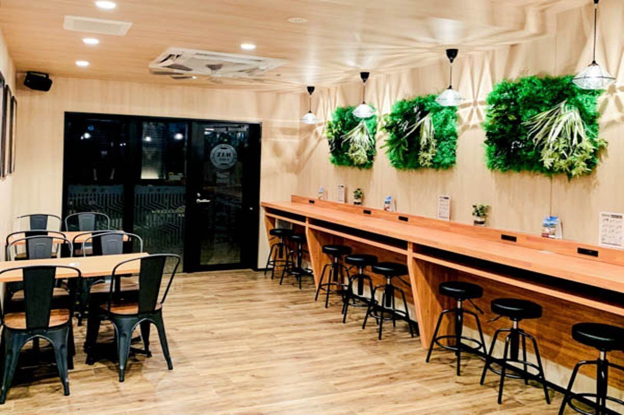 A restaurant with a long wooden counter, black bar stools, and green wall decorations.