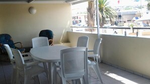 A covered patio with a round table and six chairs, a sofa, and a view of the street. - Seashells Holiday Self Catering Apartments (Jeffreys Bay)