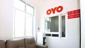 Een hotelkamer met een beige bank, een raam en een bordje met de hotelnaam 'OYO'.