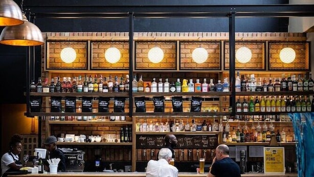 A bar area with a sign reading "Barrington's Craft Brewery". There are multiple shelves with bottles and a bar counter with stools. - Barrington's (Plettenberg Bay)