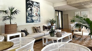 A modern living room with a large abstract painting, wicker furniture, and a ceiling fan. - Barrington's (Plettenberg Bay)