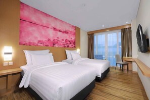 Camera d'albergo con due letti, un'opera d'arte rosa di grandi dimensioni a parete, televisore fissato al muro e vista sulla città attraverso ampie finestre.