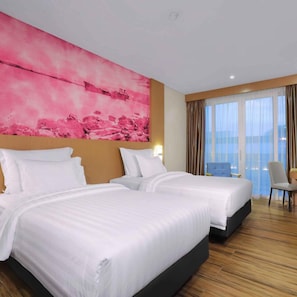 A hotel room with two beds, a large pink artwork on the wall, and a view of the sea through the windows.