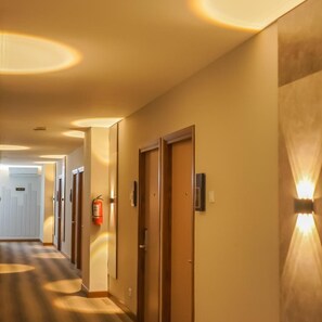 Pasillo de hotel con puertas, extintor y luces en la pared.