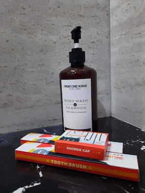A bottle of Frontone King body wash and shampoo, a shower cap, and a toothbrush on a black surface. - Front One King Hotel Tuban (Tuban)