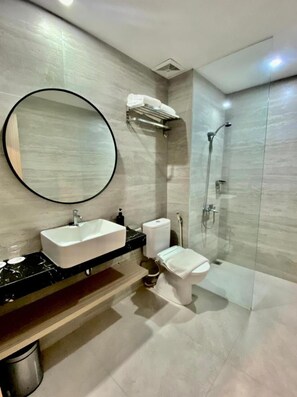 Un baño moderno con un espejo redondo, un lavabo, un inodoro y una ducha con mampara de cristal.