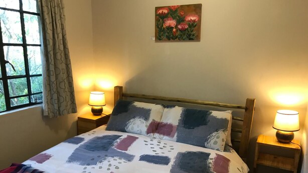 Une chambre à coucher avec un lit, deux lampes de chevet, une fenêtre avec des rideaux, un tableau au mur et une couverture à carreaux sur le lit.