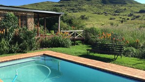 Une piscine avec une terrasse en bois, un espace salon extérieur abrité et une vue sur une colline verdoyante.