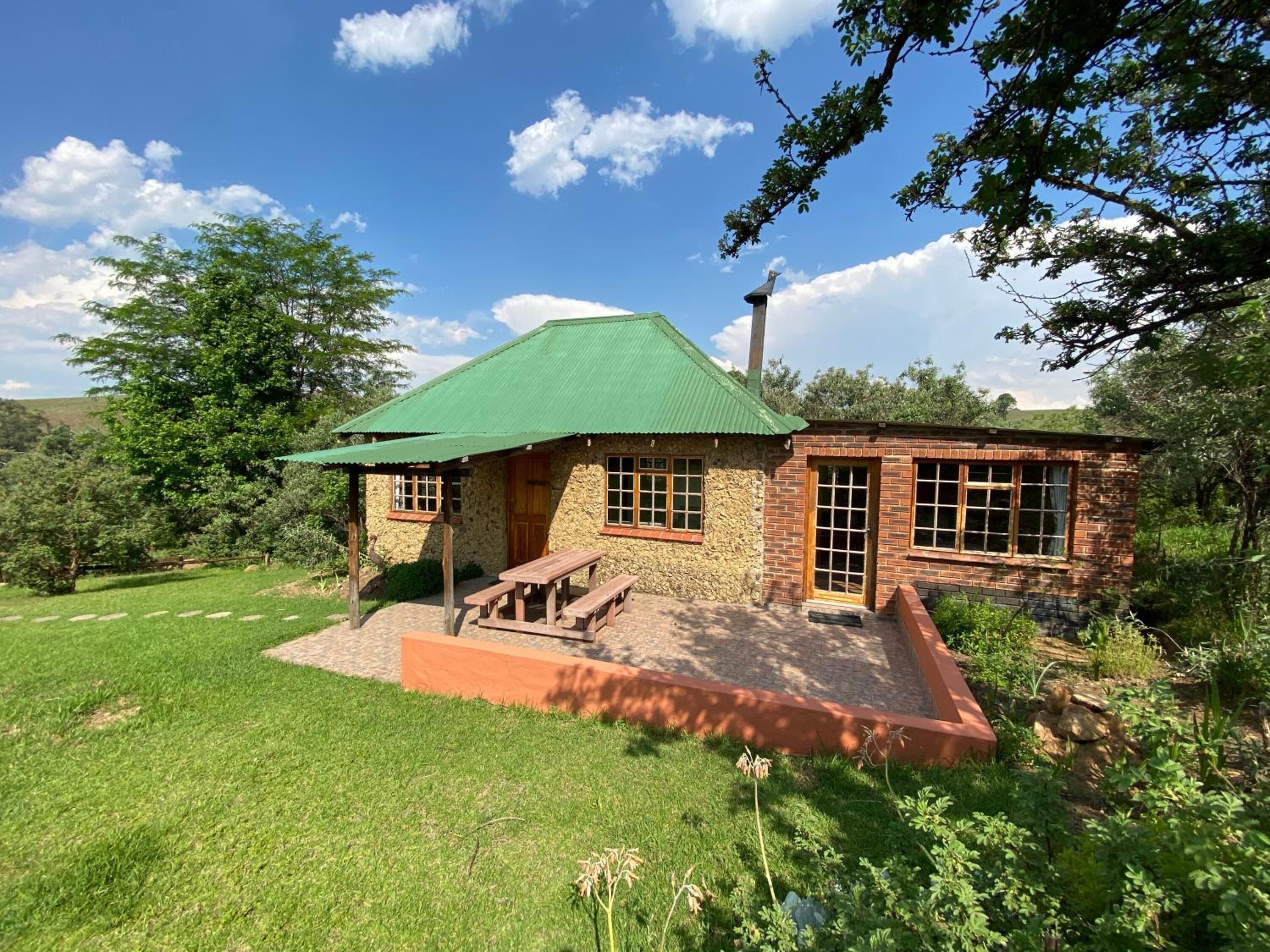 Una casa de piedra rústica con techo verde, un porche de madera y un añadido de ladrillo.
