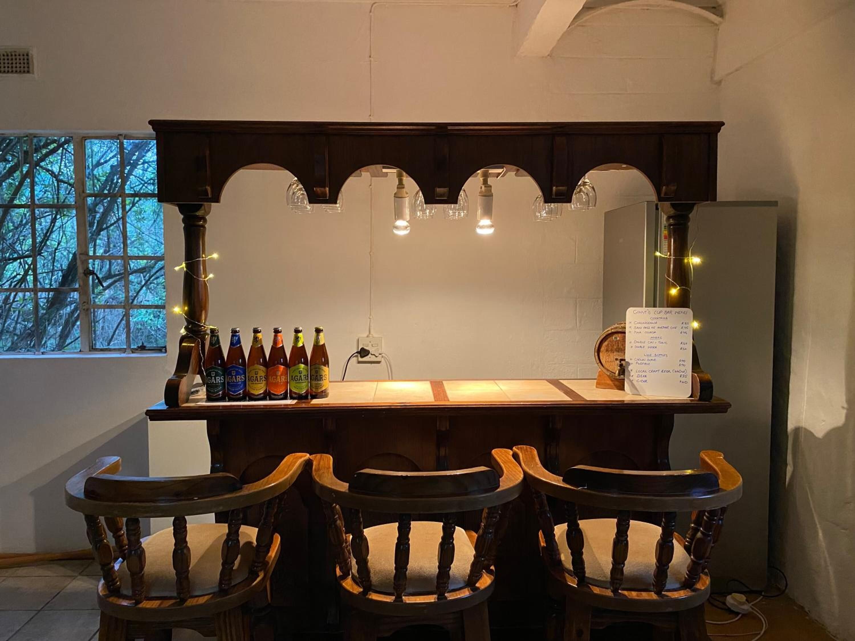 A bar area with wooden chairs, a bar counter, and bottles of beer.