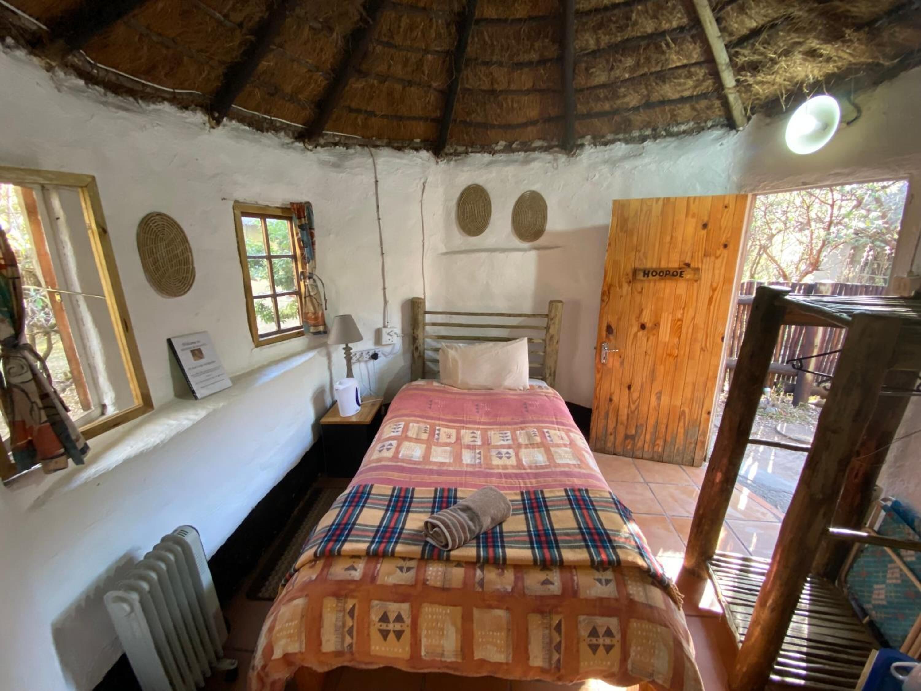 Une pièce rustique comprenant un lit, une porte en bois portant l’inscription « HOOPDE », une fenêtre et un radiateur.