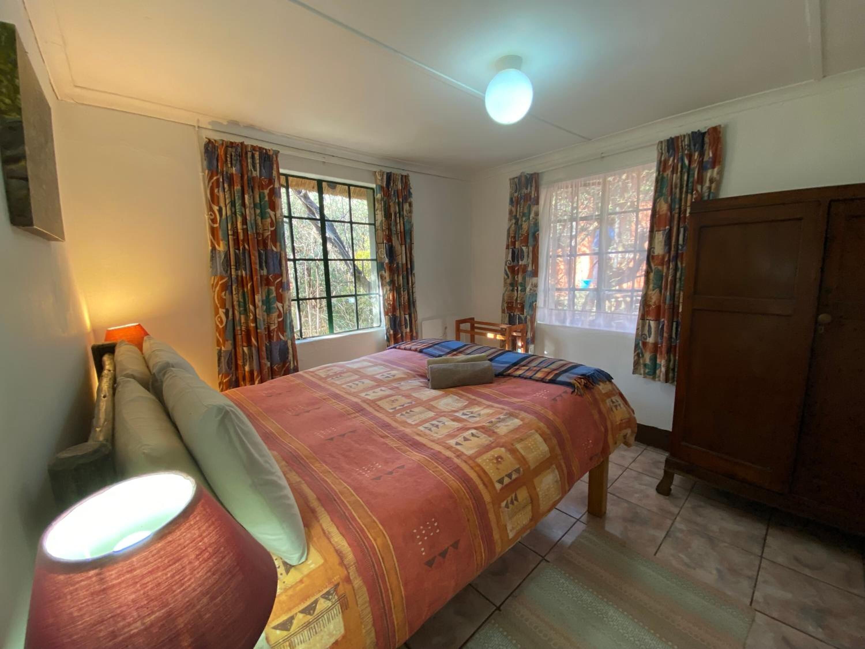 Ein Schlafzimmer mit einem Bett, Vorhängen, einem Holzschrank und einer Lampe.