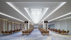 A conference room with rows of tables and chairs, a chandelier, and a carpeted floor.