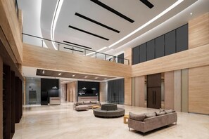 A spacious lobby with a high ceiling, modern lighting, and a seating area with sofas and a round table. - Azana Style Hotel Bandara (Tangerang)