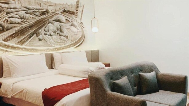 A bedroom with a bed, pillows, a red throw blanket, and a grey armchair.